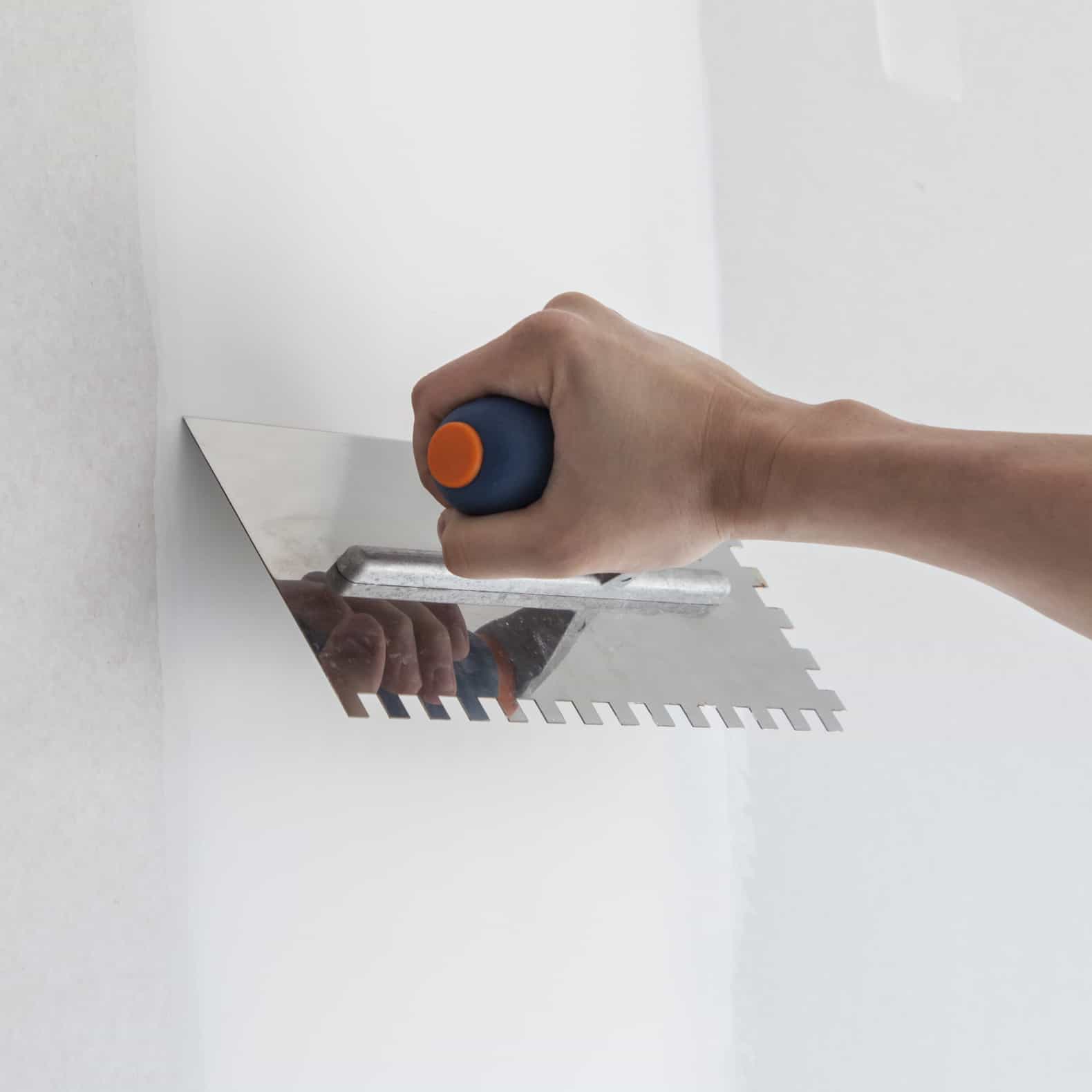 worker spreading paste on the drywall with a hand trowel