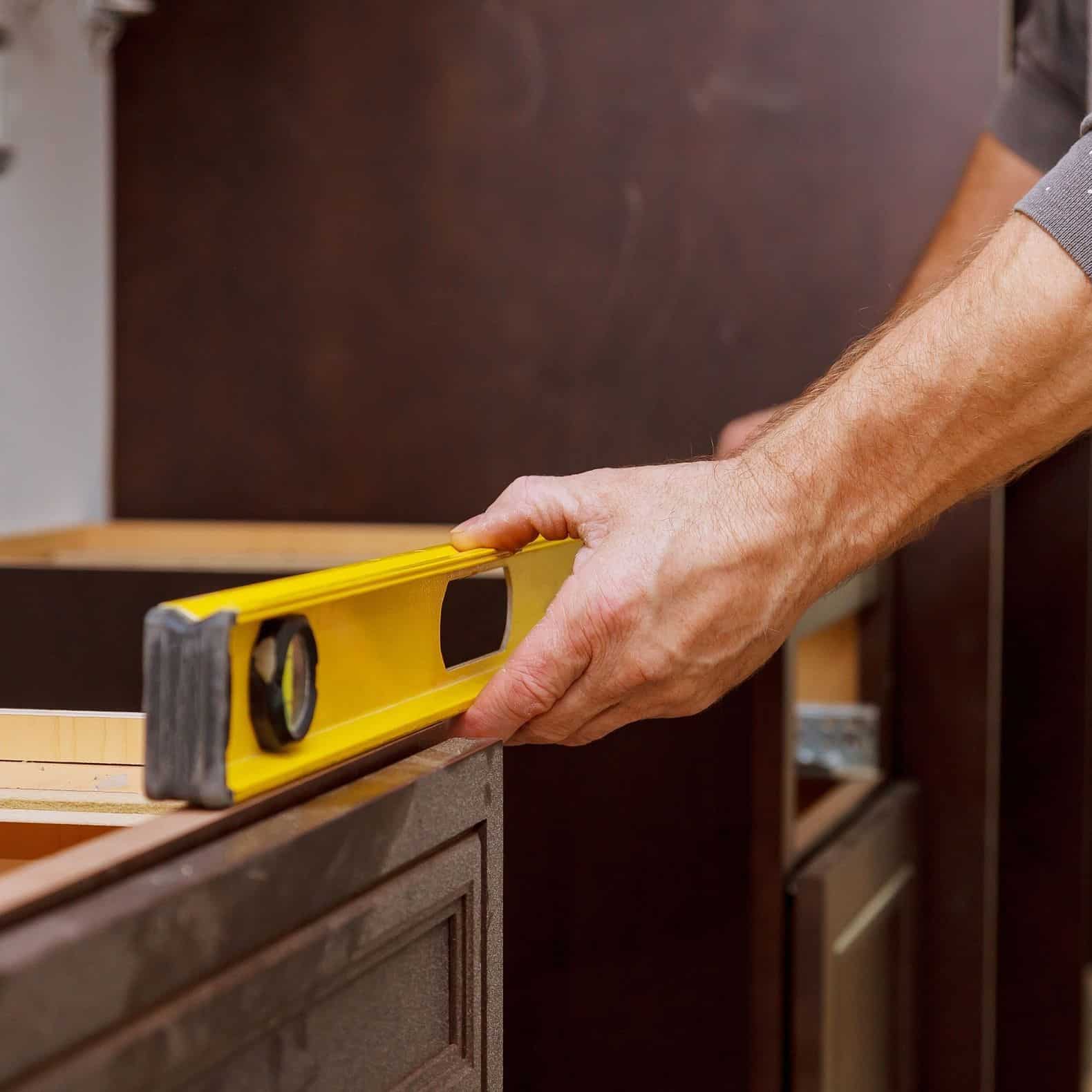 worker using yellow level on brown cabinets